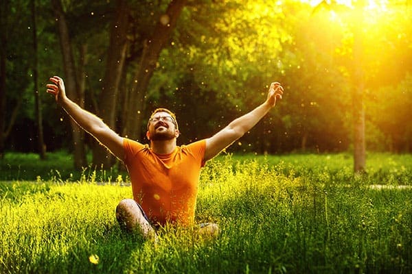 A man sitting in the grass with his arms raised.