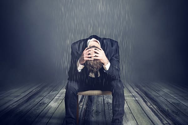 A man sitting in the rain with his head down.