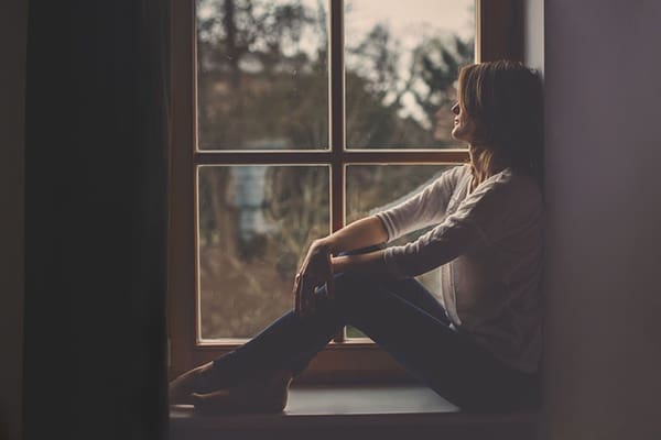 A woman sitting on the window sill looking out of a window.