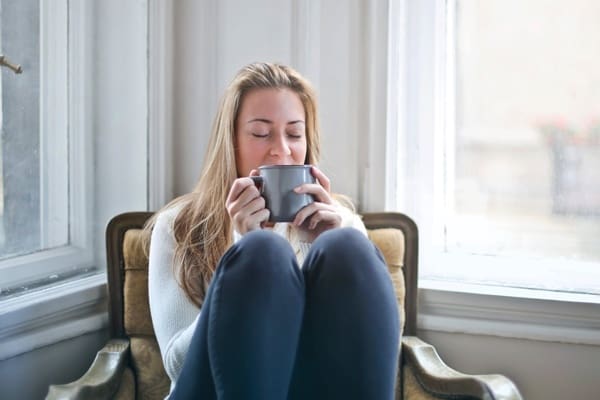 A woman sitting in a chair drinking from a cup.