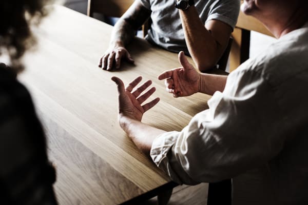 A group of people sitting at a table with one person holding his hand out.