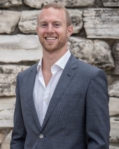 A man in a suit standing next to a stone wall.